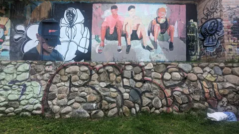 Figuras retratadas y grafiti cubren un muro de piedra.