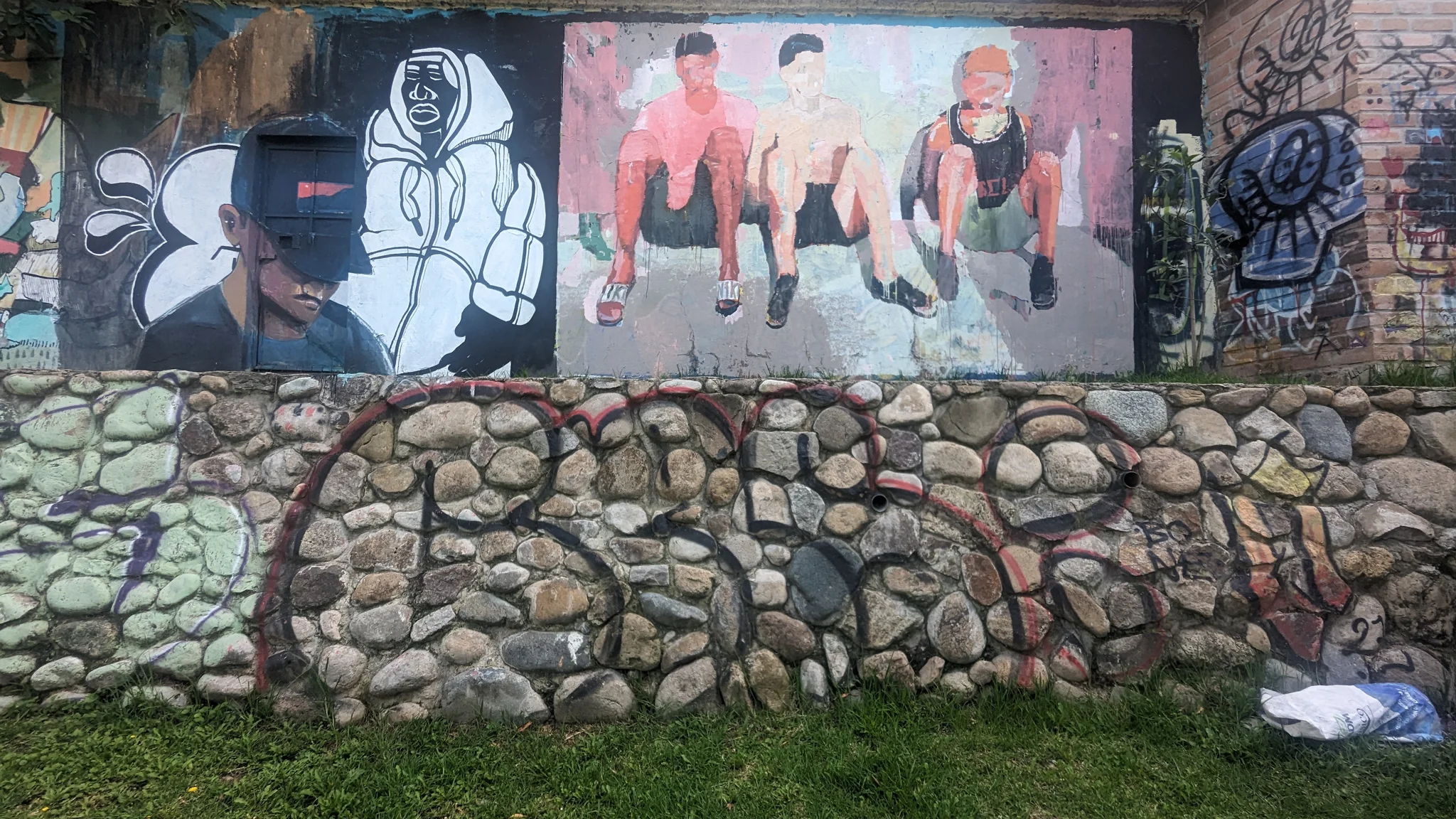 Figuras retratadas y grafiti cubren un muro de piedra.