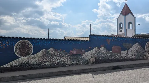 Un mural con una iglesia y figuras decorativas se extiende por un muro.