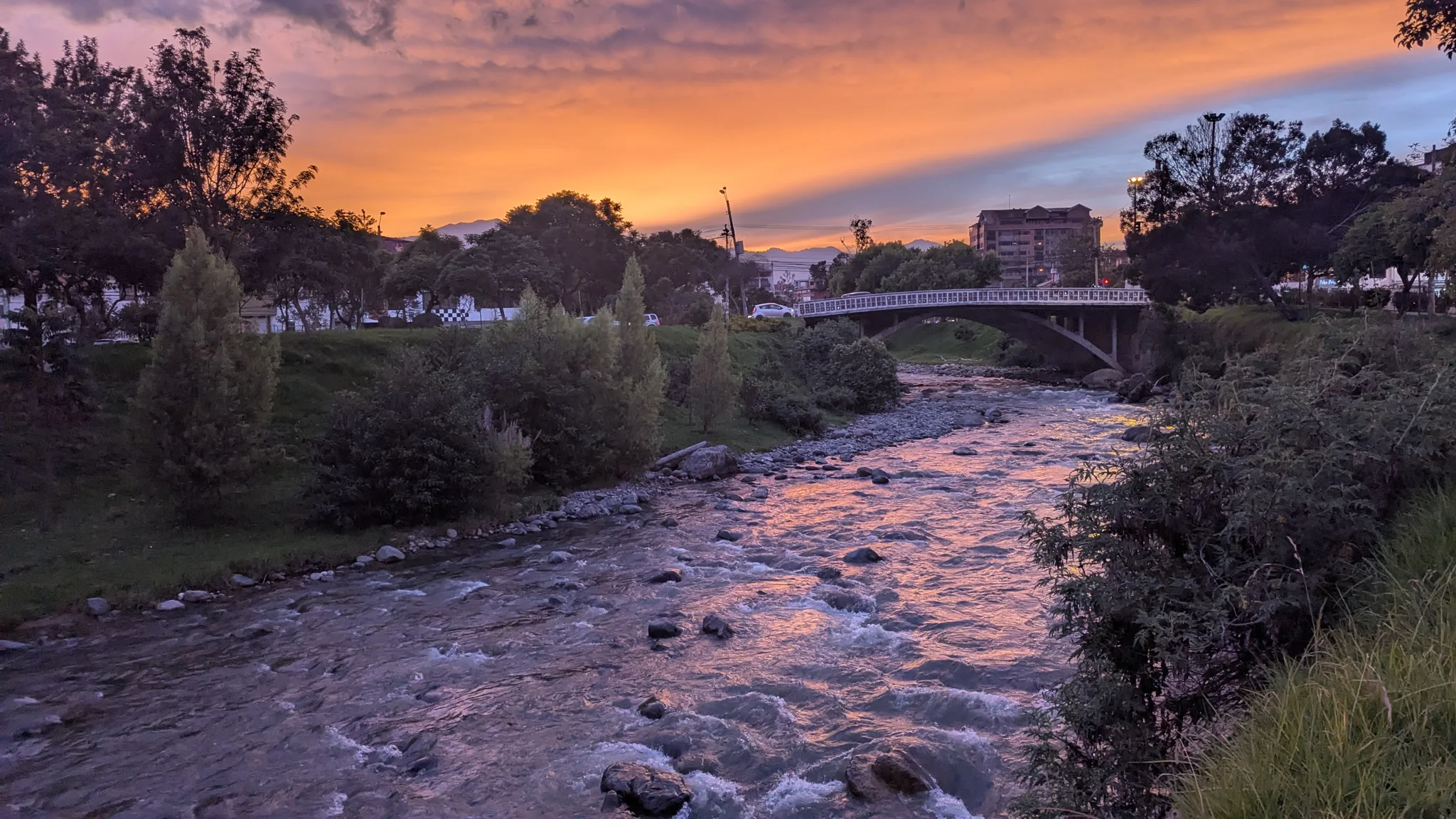 Un río rocoso refleja la luz naranja del atardecer entre árboles.