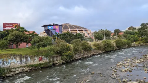 Un río pasa junto a edificios y un puente bajo un cielo nublado.