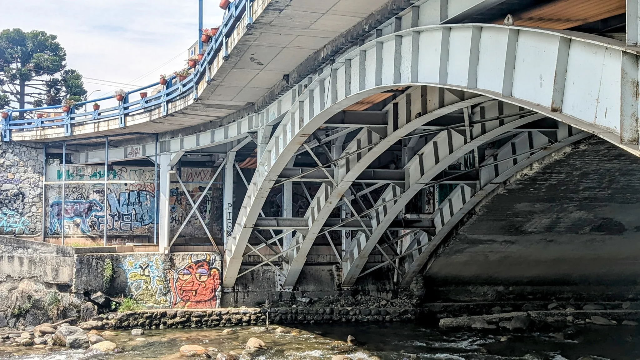 Un puente arqueado de acero cruza un río en un entorno urbano.