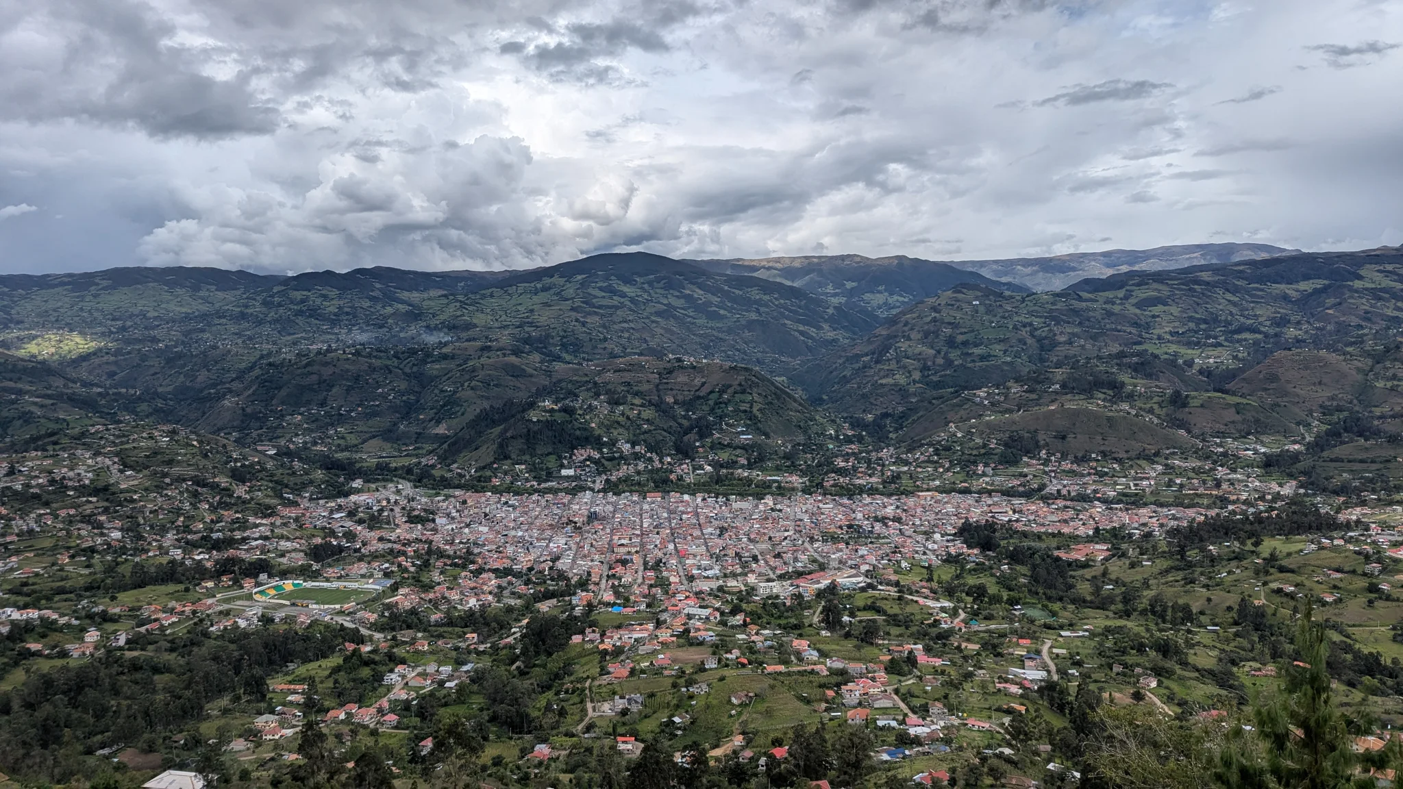 Un valle urbano se extiende bajo lomas verdes y un cielo nublado.