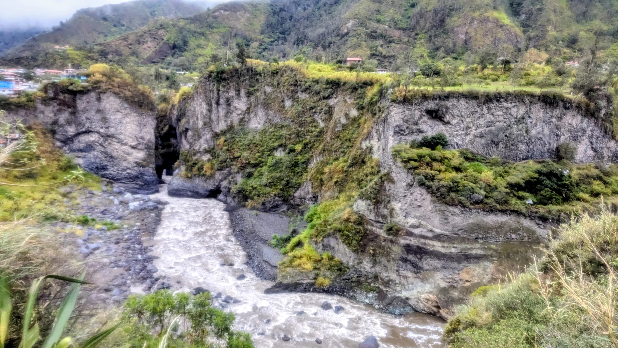 El agua cae sobre rocas estratificadas en un valle verde de altura.