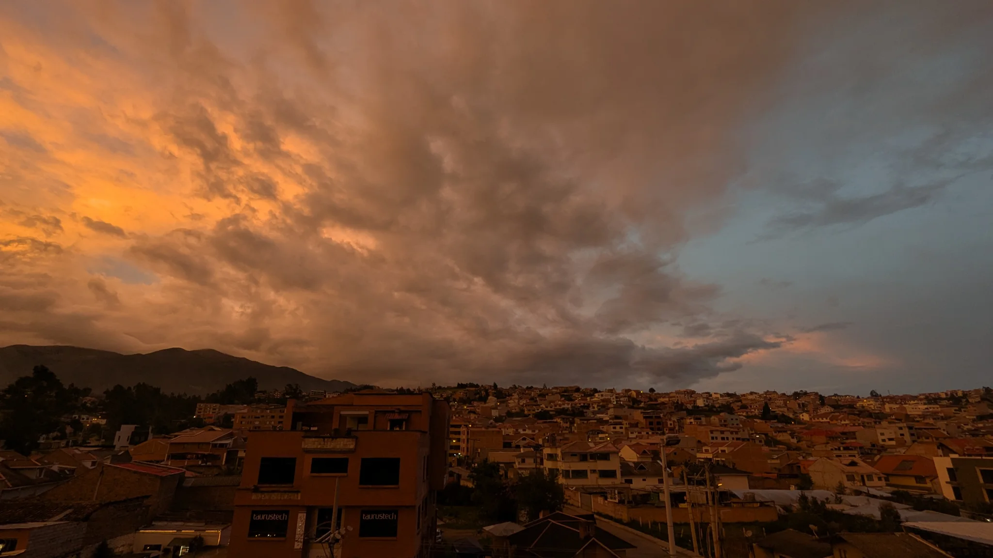 Nubes de tormenta naranjas brillan sobre lomas y tejados de la ciudad.