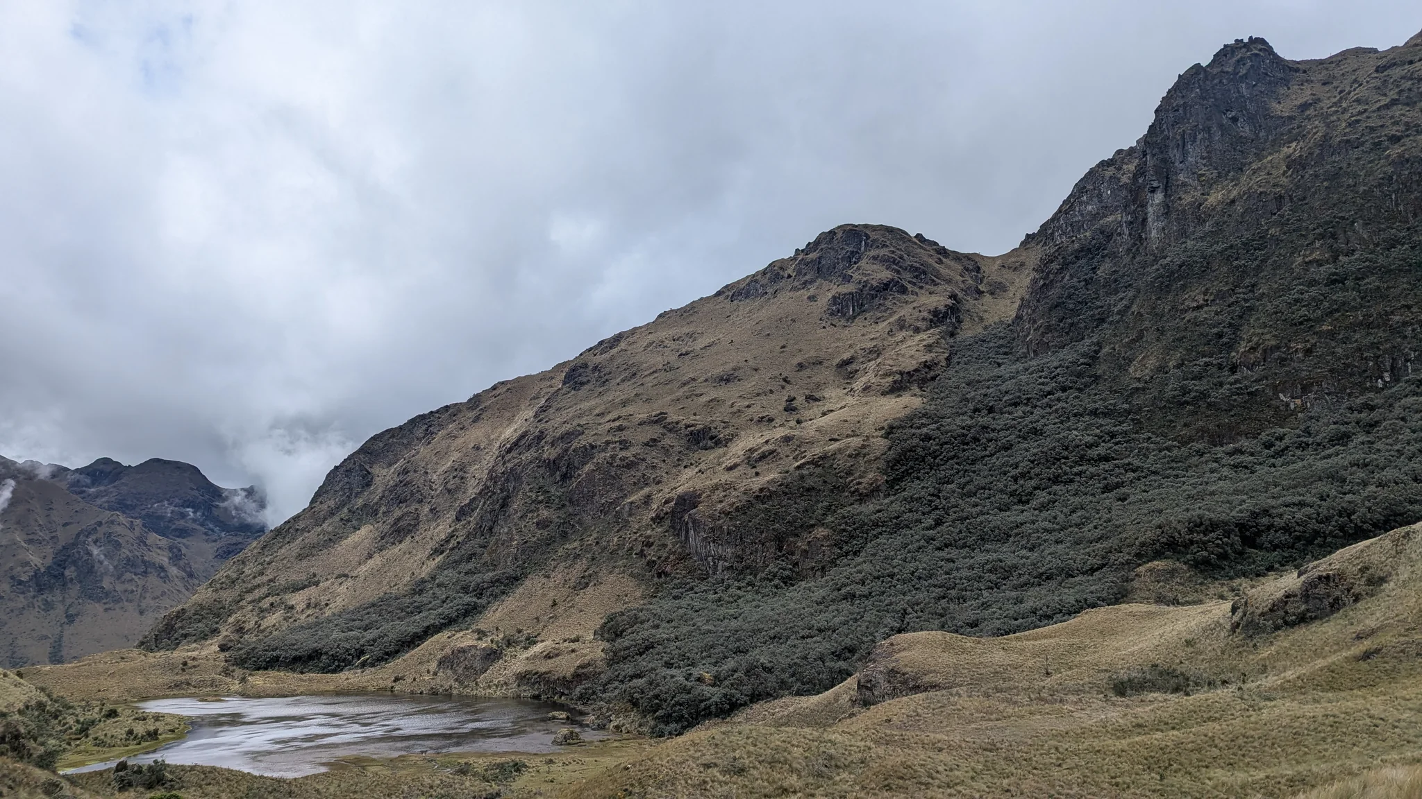 La laguna Barrancos se extiende entre márgenes someros expuestos, laderas boscosas y filos de roca oscura.