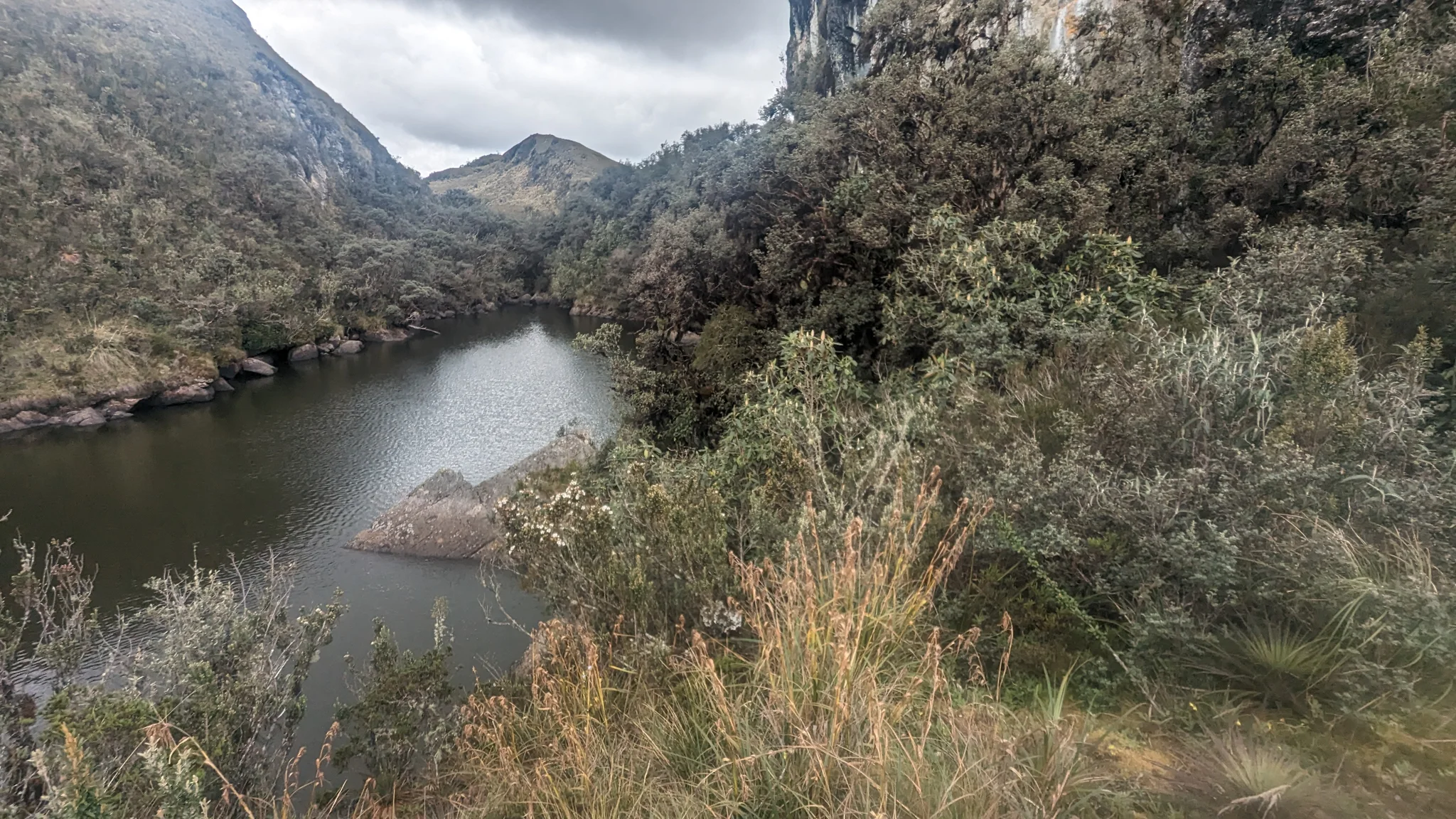 Una laguna estrecha entre laderas arbustivas. El nombre del cuerpo de agua sigue sin confirmarse.