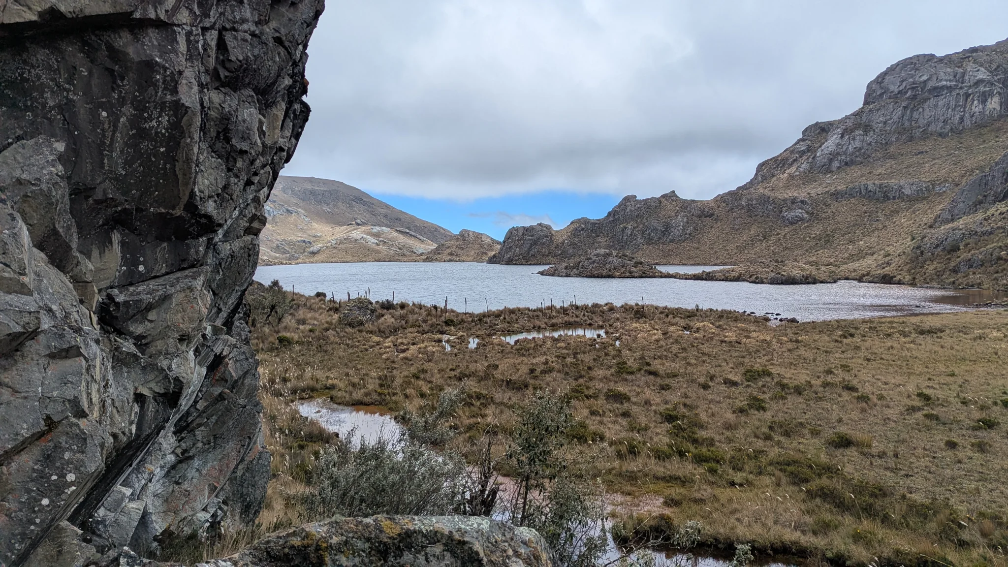 Una pared oscura en primer plano enmarca Estrellascocha de Quitahuaycu y el pajonal abierto de su orilla.