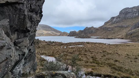 Una pared oscura en primer plano enmarca Estrellascocha de Quitahuaycu y el pajonal abierto de su orilla.