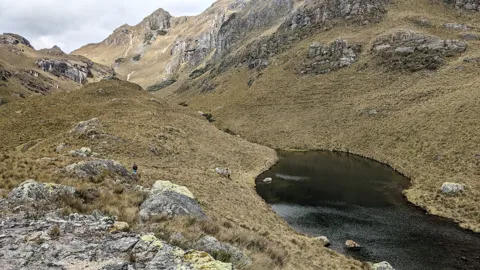 Una laguna redondeada bajo cumbres. El nombre del cuerpo de agua sigue sin confirmarse.