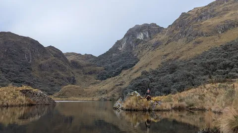 Un caminante reflejado junto a una laguna alta. El nombre del cuerpo de agua sigue sin confirmarse.