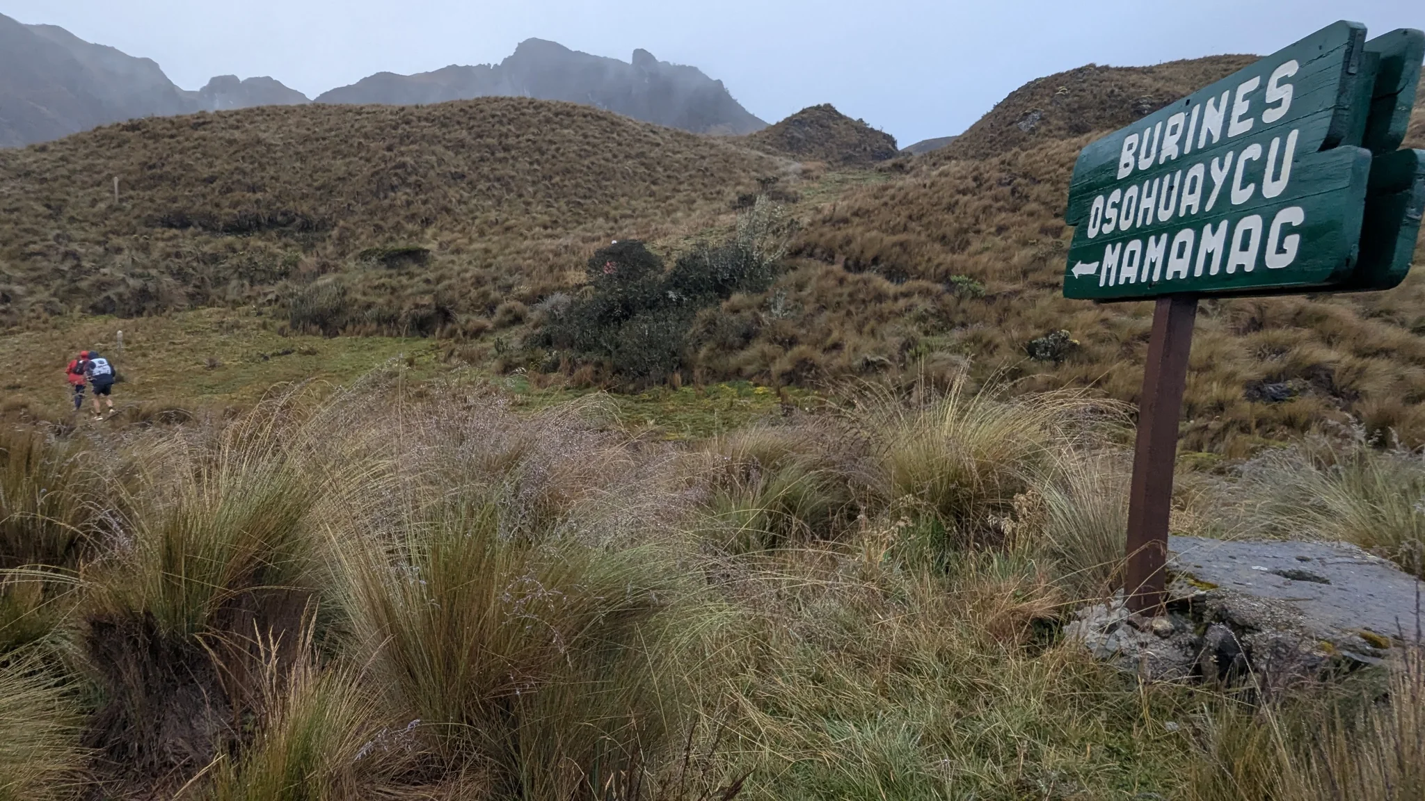 Un letrero de madera señala Burines, Osohuaycu y Mamamag junto a un sendero estrecho de páramo.