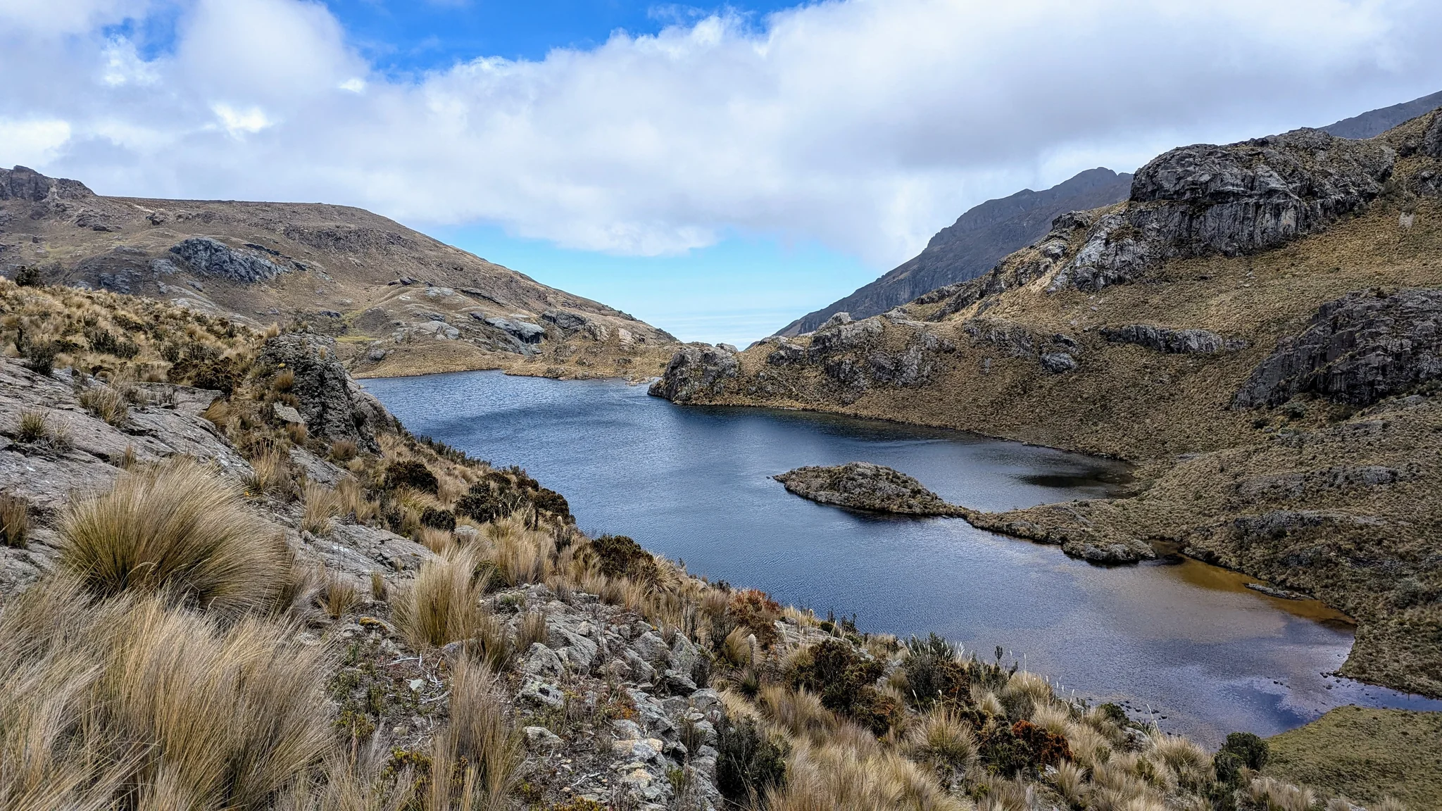 Estrellascocha de Quitahuaycu se curva alrededor de una península rocosa bajo laderas abiertas de altura.