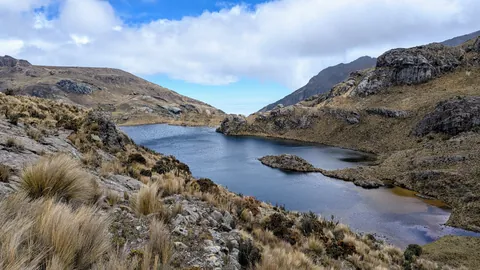 Estrellascocha de Quitahuaycu se curva alrededor de una península rocosa bajo laderas abiertas de altura.