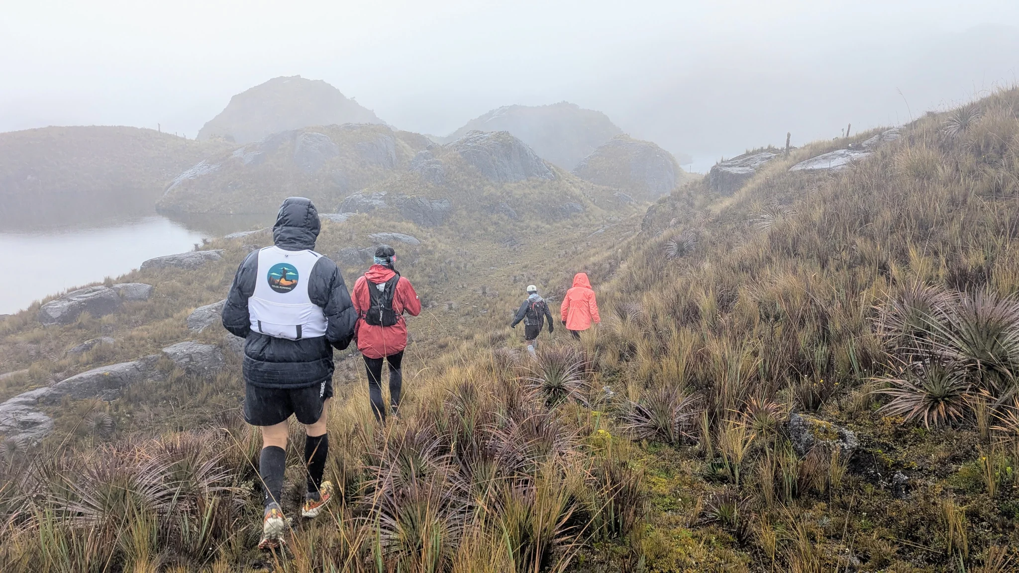 Caminantes con capucha sobre una laguna con niebla. El nombre del cuerpo de agua sigue sin confirmarse.